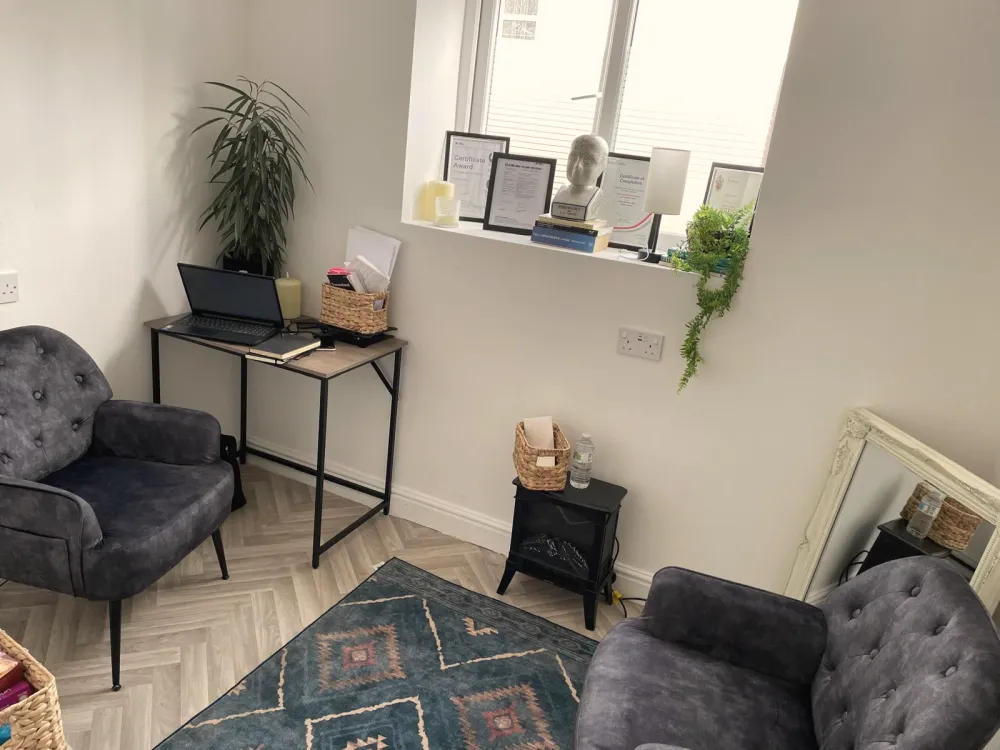 Andrea’s therapy room at Douglas House, with two grey armchairs, a patterned rug, a small desk and a window